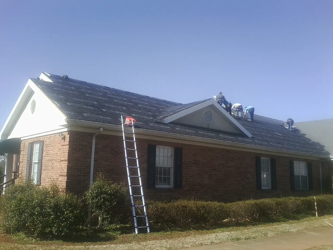 Crew tearing shingles off a brick ranch roof with a ladder set — Metal Roof Repair work by our crew in Nehawka