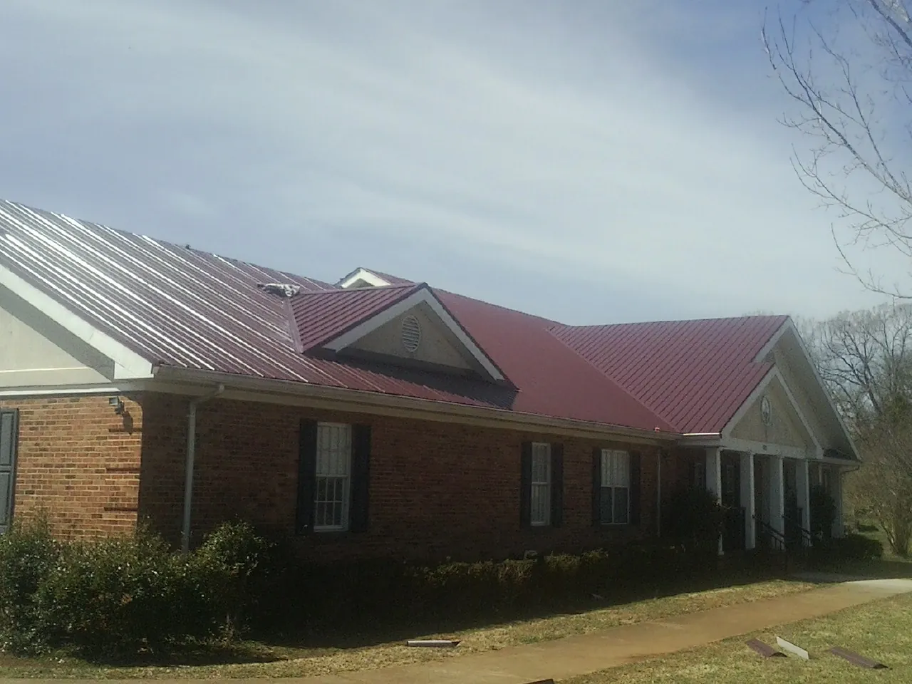 Red metal roof with gabled entries on a long brick building, from a Hail Damage Roof Repair job in Nehawka