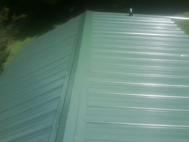 New green metal panels meeting at the ridge of a roof — Flat Roof Repair work by our crew in Nehawka