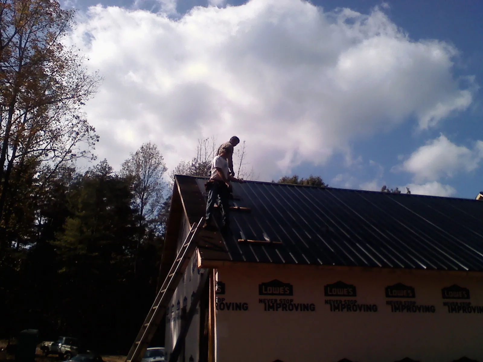 Roofer fastening dark metal panels high against a cloudy sky, from a Roof Inspection job in Nehawka