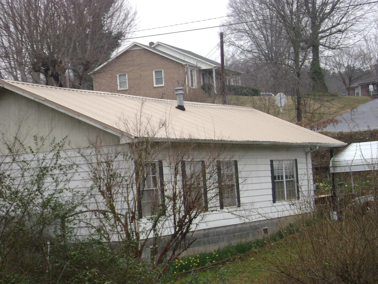 Tan metal roof on a white sided house set into a hillside — Commercial Roofing by Roofing Brothers in Nehawka